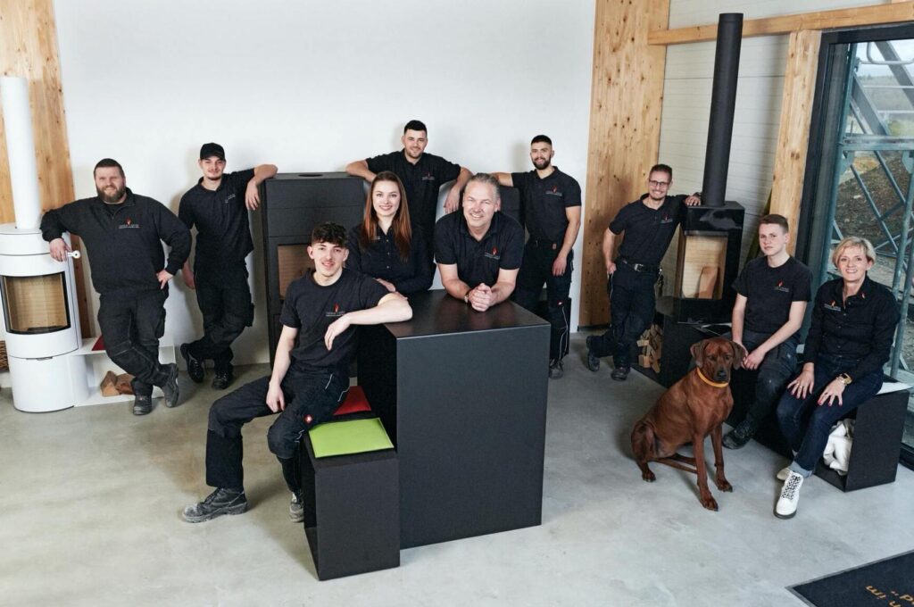 Teamfoto mit 10 Personen in schwarzen T-Shirts vor Ofen Ausstellungsstücken